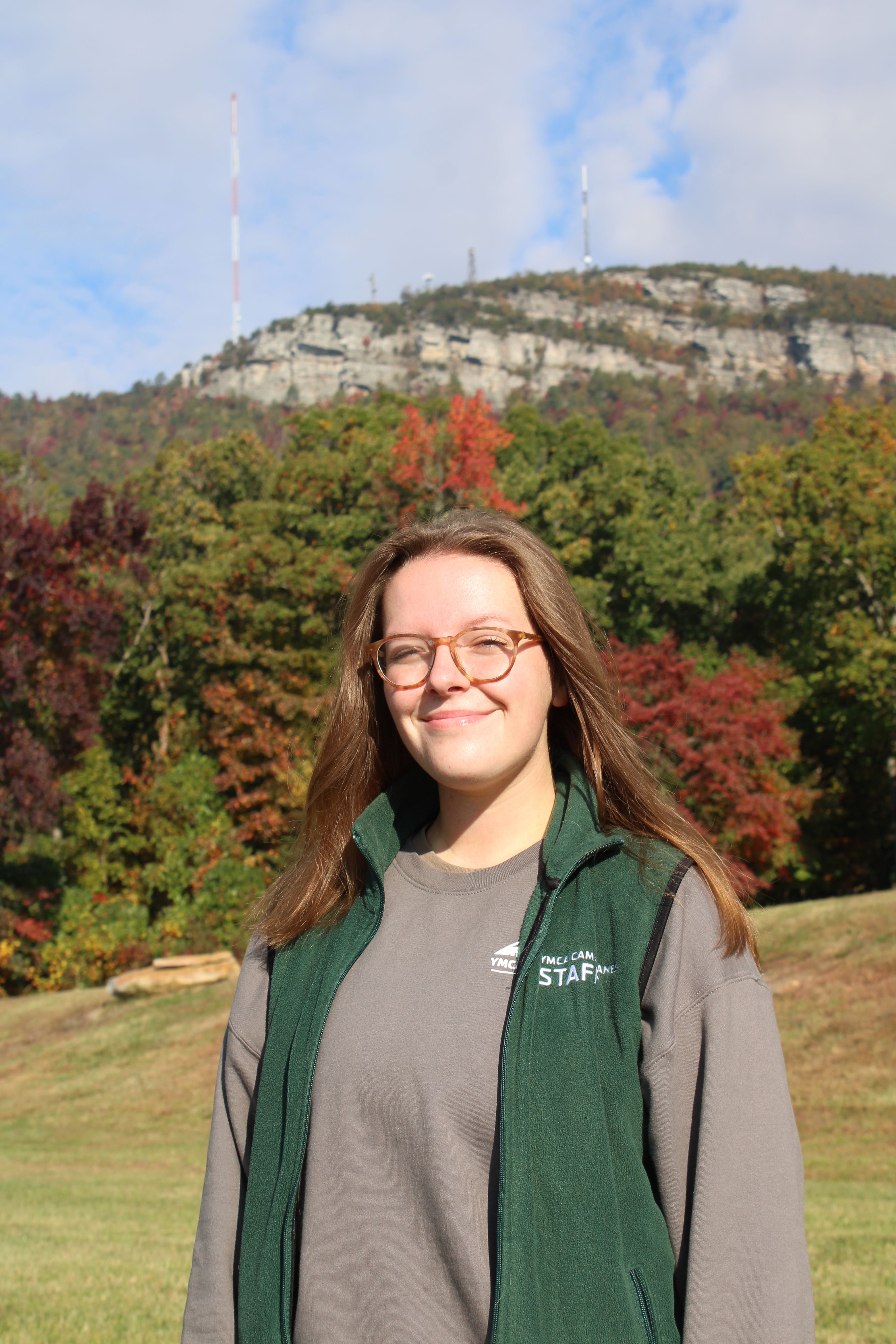 Blond girl in front of mountain in green vest