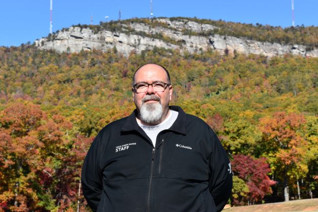 Man in front of mountain with green vest